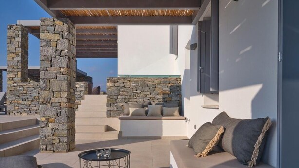 An outdoor patio area with stone columns, a cushioned seating area, and a round table. - OLEA VILLA (NAOUSA)