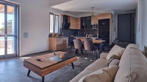 A modern living room with a sofa, a coffee table, and a dining area with chairs and a table. - OLEA VILLA (NAOUSA)