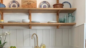 A kitchen with wooden shelves, a stainless steel dishwasher, and a patterned rug.