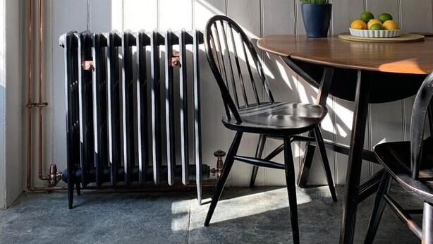A dining area with a table, chairs, a radiator, and shelves with plates.