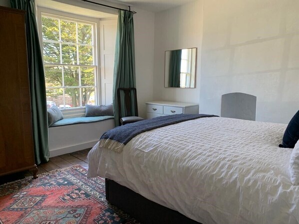 Une chambre avec un grand lit, une fenêtre avec des rideaux, une table de chevet et un miroir au mur.