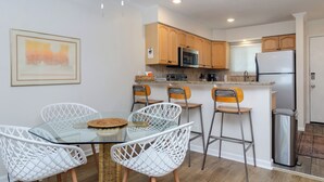 Une cuisine moderne avec des meubles blancs, un réfrigérateur en acier inoxydable et une table à manger en verre, assortie de chaises blanches.