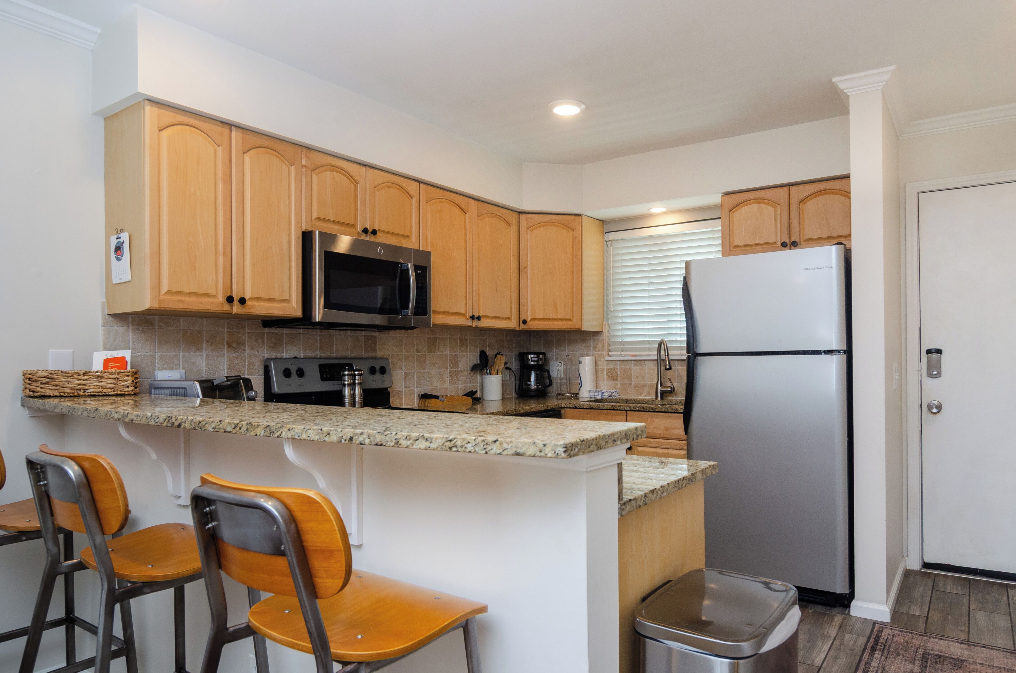 A kitchen with wooden cabinets, a stainless steel refrigerator, a microwave, and a granite countertop.