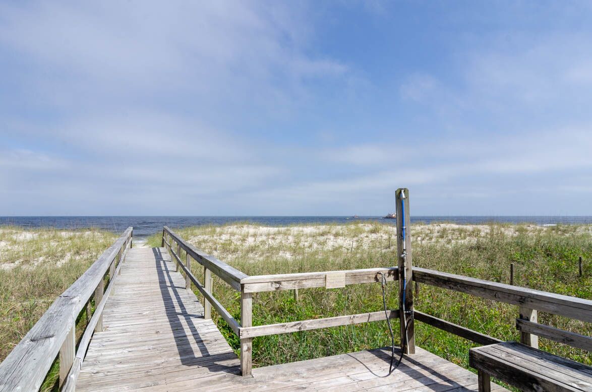 A wooden boardwalk leading to the beach with a bench and a sign on the right.