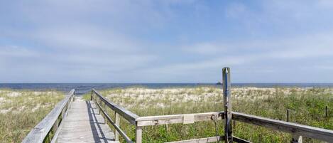 A wooden boardwalk leading to the beach with a bench and a sign on the right.