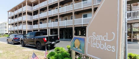 A multi-story hotel with balconies, a sign reading "Sand Pebbles", and American flags in the foreground.