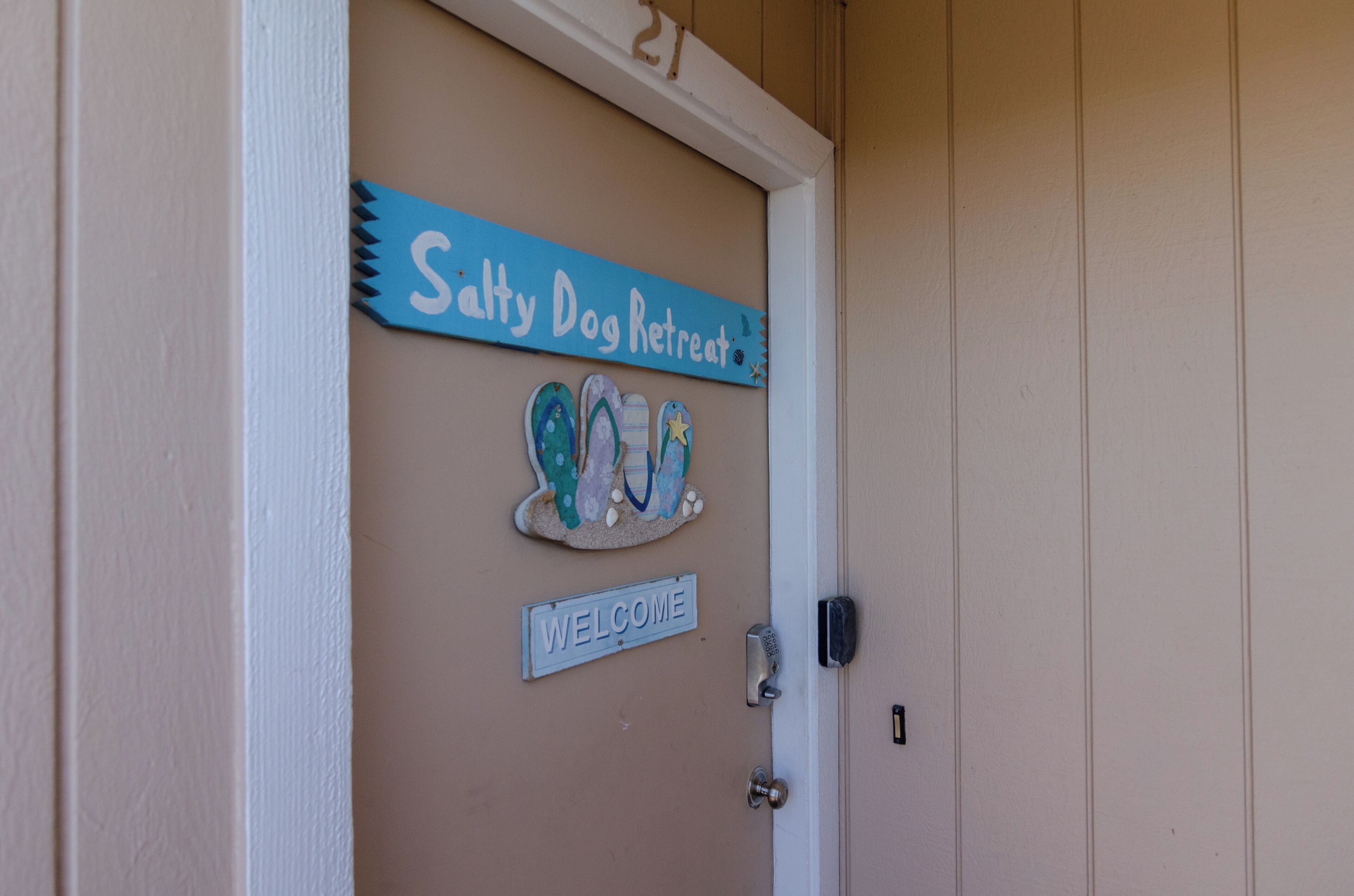 Una puerta con un letrero que dice 'Salty Dog Retreat', un cartel de bienvenida y el número '21' encima.