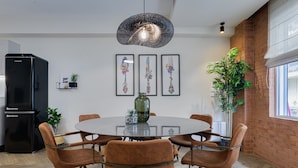 Un coin repas comprenant une table ronde, six chaises, un réfrigérateur noir et trois œuvres d’art encadrées accrochées au mur.