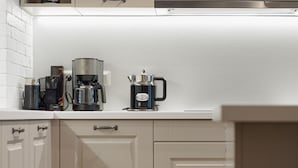 Une cuisine avec des meubles blancs, une machine à café et une bouilloire posées sur le plan de travail.
