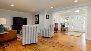 A spacious living room with hardwood flooring, a flat-screen TV, striped armchairs, a sofa, and a coffee table. - Historic Cottage in the heart of Pinehurst Village (Pinehurst)