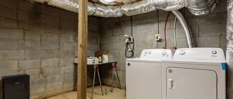 Une buanderie équipée d’un lave-linge et d’un sèche-linge, dotée de conduits d’aération isolés et comprenant une petite table où sont rangés les produits de nettoyage.