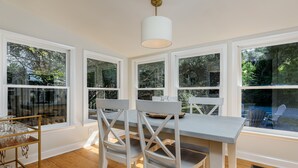A dining area with a table and chairs, large windows, and a hanging light fixture. - Historic Cottage in the heart of Pinehurst Village (Pinehurst)