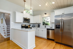A modern kitchen with white cabinetry, a stainless steel refrigerator, and a wooden island.