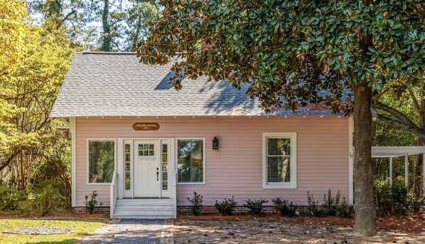 A pink house named "The Pink Cottage" with a white door, two windows, and a small porch.