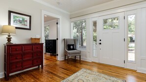 A room with hardwood flooring, a red dresser, a grey armchair, and a patterned rug. - Historic Cottage in the heart of Pinehurst Village (Pinehurst)