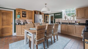 Une cuisine avec des meubles de rangement en bois, une table à manger avec des chaises en osier et un luminaire suspendu.