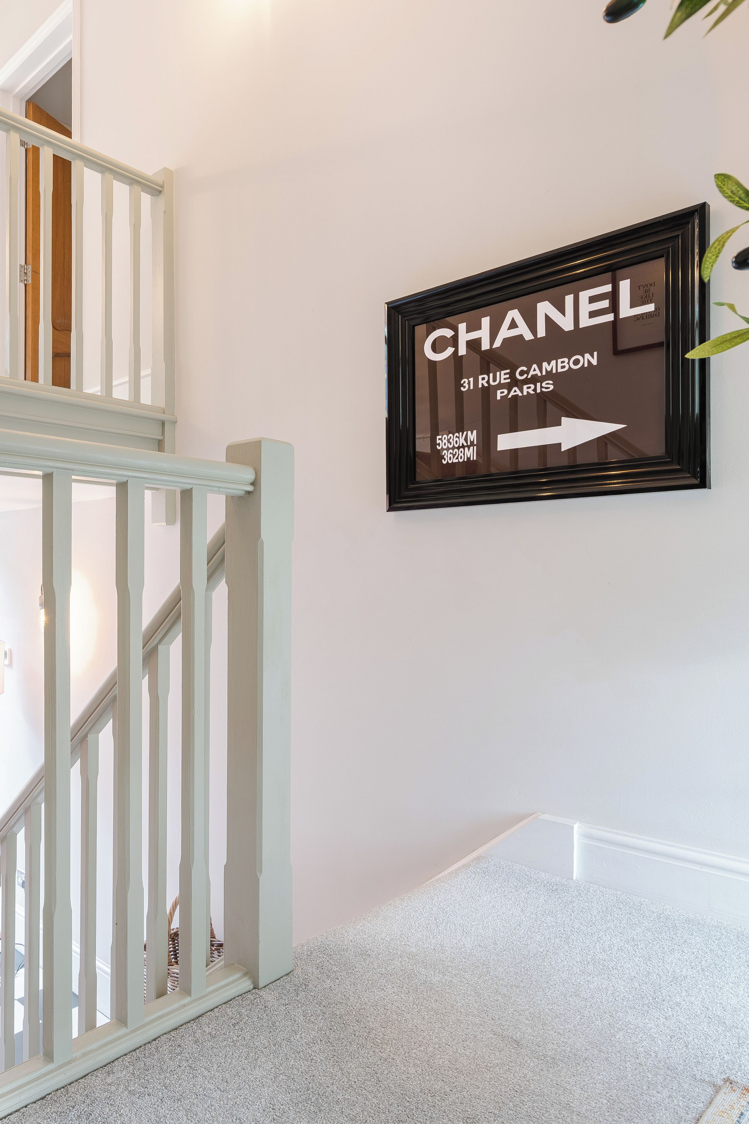 A framed sign on a wall with the text "CHANEL 31 RUE CAMBON PARIS" and an arrow pointing right.