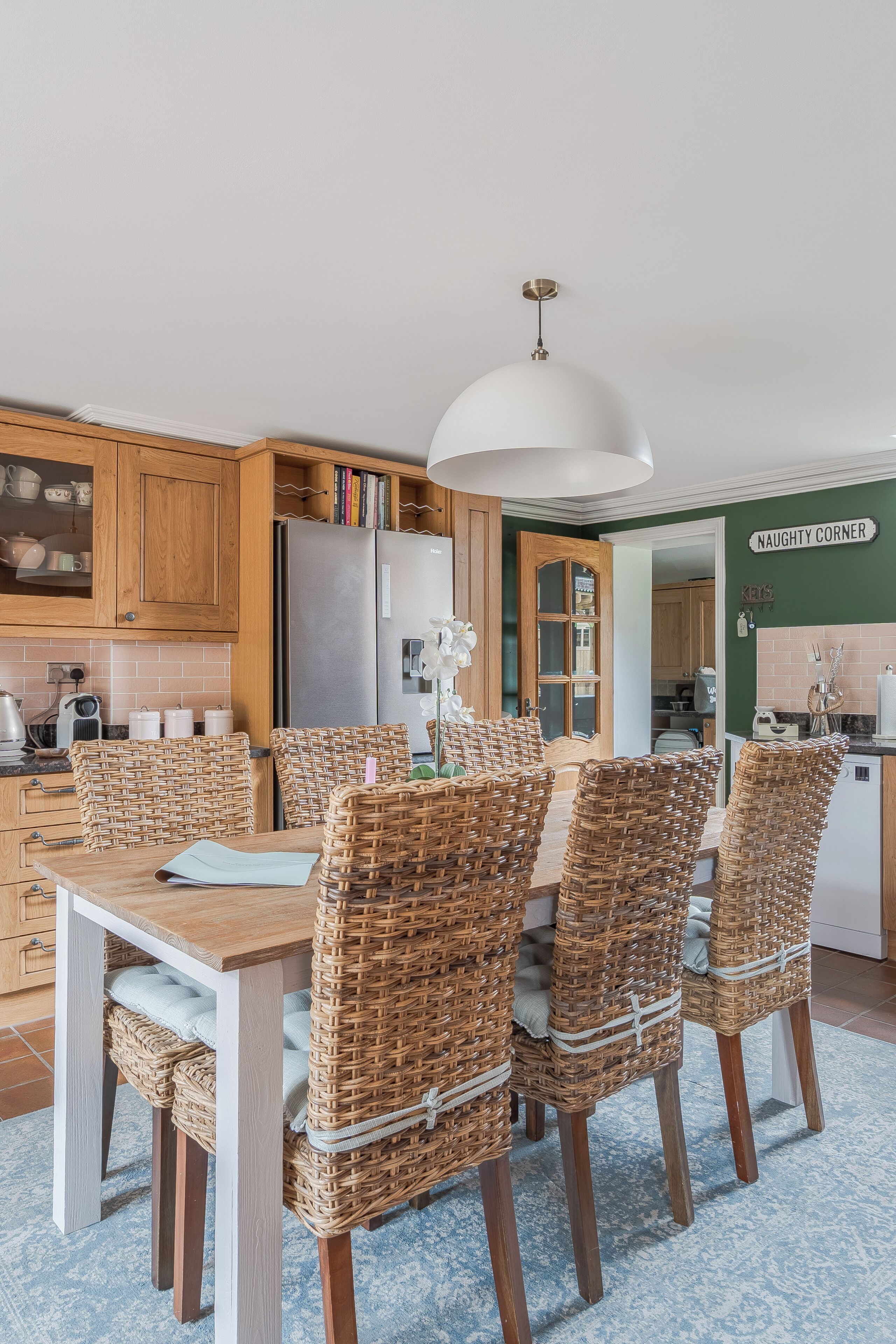 A kitchen with wooden cabinets, a stainless steel refrigerator, wicker chairs, and a white pendant light.