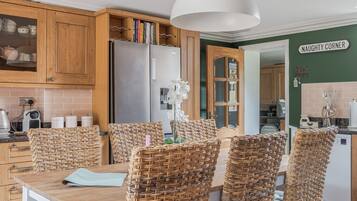 A kitchen with wooden cabinets, a stainless steel refrigerator, wicker chairs, and a white pendant light.