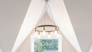 Une pièce avec un plafond blanc, une fenêtre ornée de rideaux roses et un lustre doté de plusieurs ampoules.