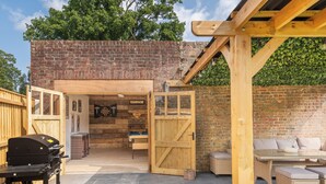 Un espace extérieur aménagé en terrasse, avec un mur en briques, une pergola en bois et un coin salon doté de meubles en osier.