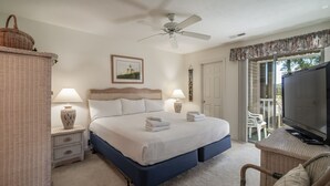 Un dormitorio con cama, dos mesitas de noche, ventilador de techo, televisor y ventana con cortinas.