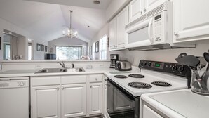 Una cocina moderna con armarios blancos, horno empotrado, estufa con cuatro quemadores y cafetera.