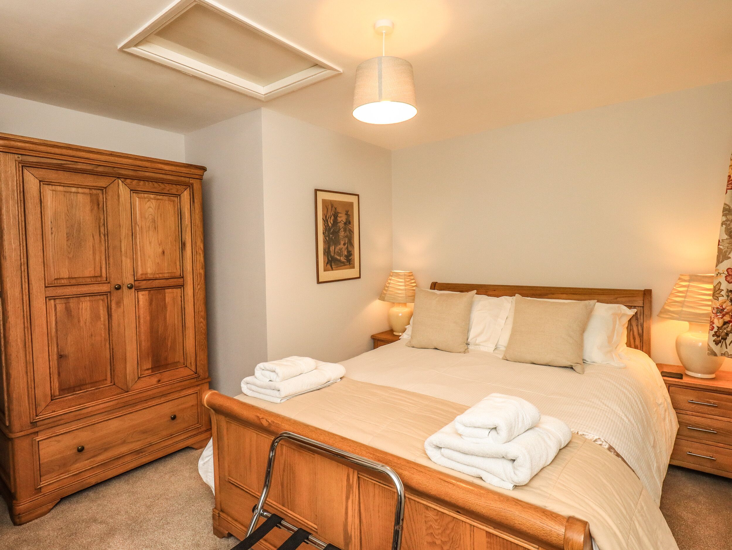 A bedroom with a wooden wardrobe, a bed with white bedding, a bedside table with a lamp, and a picture on the wall.