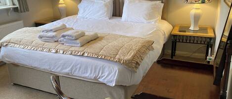 A neatly made bed with white linens, two bedside lamps with floral patterns, a wooden nightstand, and a chair with a floral cushion.
