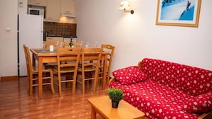 A small, cozy living area with a wooden dining table and chairs, a red sofa, and a small table with a plant. - 300m from ski slopes, Ground floor, swimming pool, sauna, balcony, parking, tv, ski locker, 30m² (Le Dévoluy)