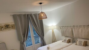 Ett sovrum med två sängar, en stol, en lampa och ett fönster med gardiner.