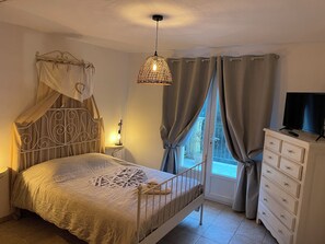 A bedroom with a bed, a bedside lamp, a TV on a dresser, and a window with curtains.