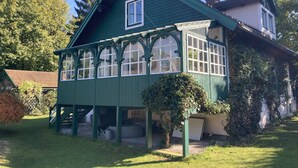 Ein grünes Haus mit einer großen Veranda, einem überdachten Eingangsbereich und einem kleinen Garten.