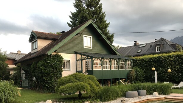 Ein Haus mit einem grünen Dach, einem Teich im Vordergrund und einem gepflegten Garten.