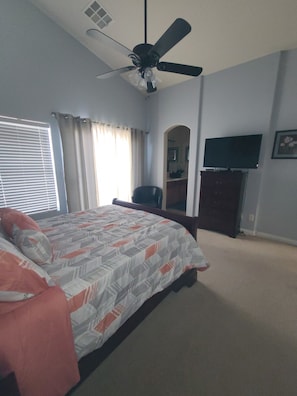 A bedroom with a bed, a ceiling fan, a TV, and a window with curtains.
