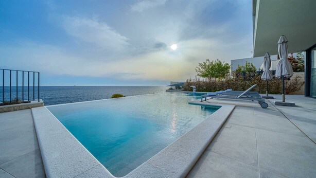 A infinity pool with a view of the ocean, outdoor seating, and umbrellas. - Villa Valiosa - stunning beachfront villa with a pool and a sauna for ten guests by MyWaycation (Rogoznica)