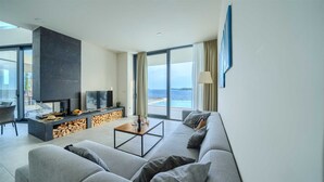 A modern living room with a large TV, a fireplace, a sofa, and a view of the sea. - Villa Valiosa - stunning beachfront villa with a pool and a sauna for ten guests by MyWaycation (Rogoznica)