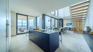 A modern kitchen with a large island, a dining area with a view, and a staircase with wooden slats. - Villa Valiosa - stunning beachfront villa with a pool and a sauna for ten guests by MyWaycation (Rogoznica)