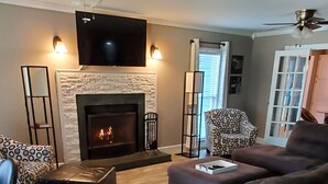 A living room with a fireplace, a television mounted above it, and a patterned armchair.