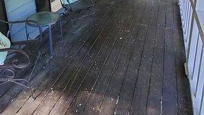 A covered porch with dark wooden flooring, metal chairs, and a small table.
