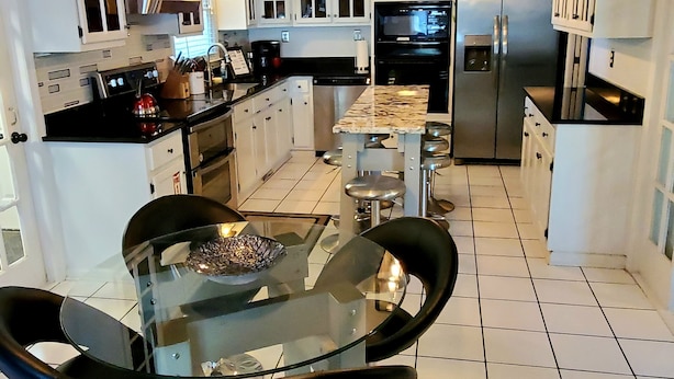 A modern kitchen with a glass dining table, black chairs, and stainless steel appliances.