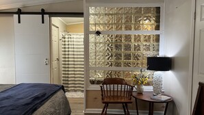 A bedroom with a bed, a wooden chair, a small table with a lamp, and a window with decorative glass panels.