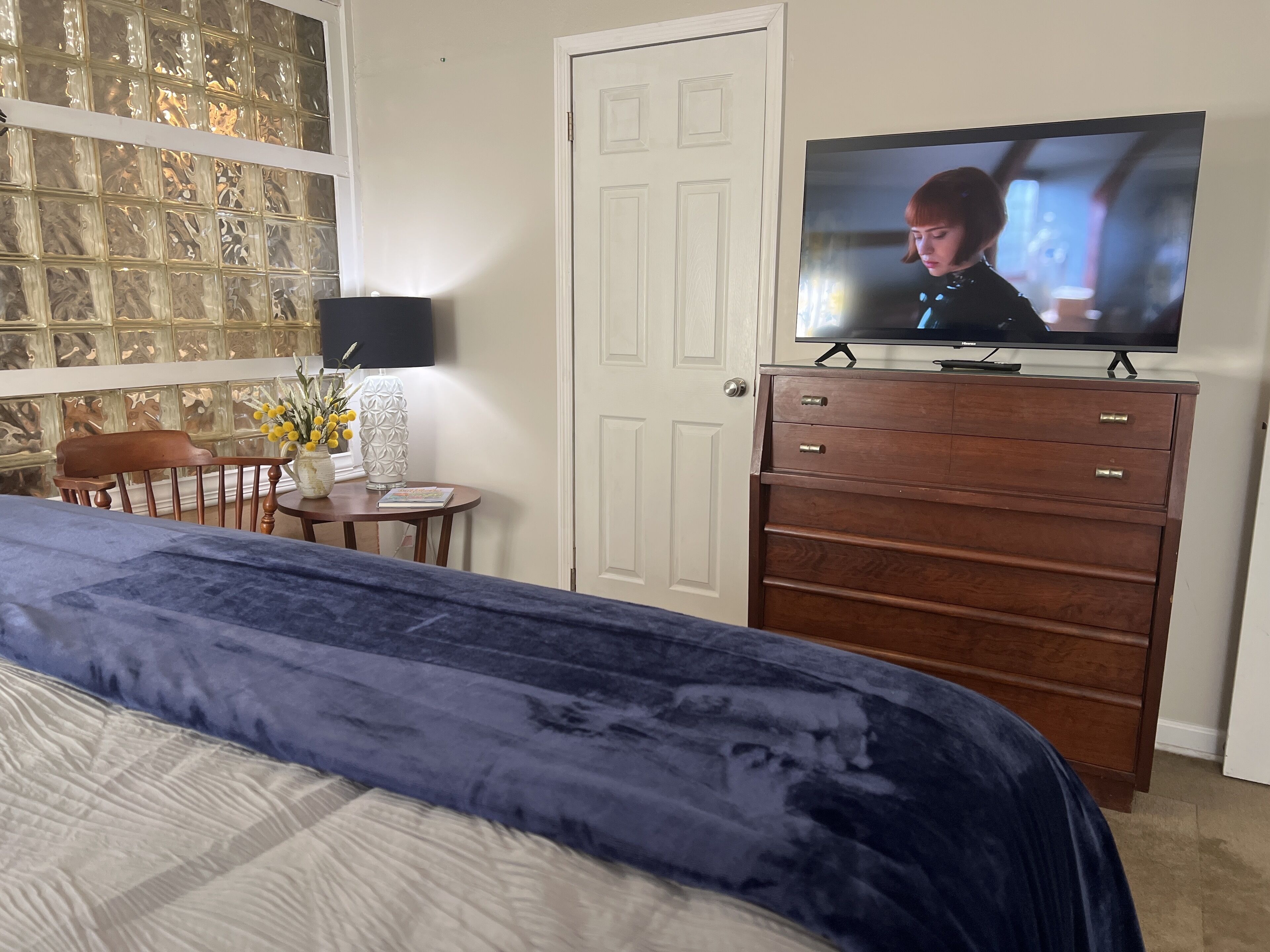A bedroom with a bed, dresser, TV, and a decorative wall.
