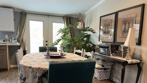 A dining area with a round table, chairs, a potted plant, and a side table with a lamp and decorative items.
