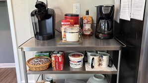 A kitchen counter with a coffee maker, a jar of cream, a bottle of liquor, and a coffee pot.
