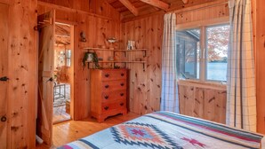 Une chambre dans une cabane en bois, avec un lit, une commode et une fenêtre donnant sur un plan d’eau.