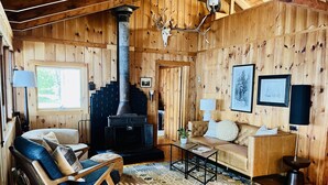 L’intérieur d’un chalet chaleureux, avec une cheminée, des murs en bois, un canapé, un fauteuil et un tapis.