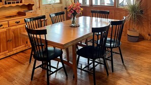 Une salle à manger en bois, avec une grande table et des chaises, un lustre et une bibliothèque remplie de livres.