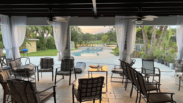 A covered patio with outdoor seating, a pool, and a view of the surrounding greenery. - Tampa River Oasis (Tampa)