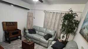 Ein Wohnzimmer mit Ecksofa, einer Holzbalkenbar, einem Deckenventilator und einer Topfpflanze.